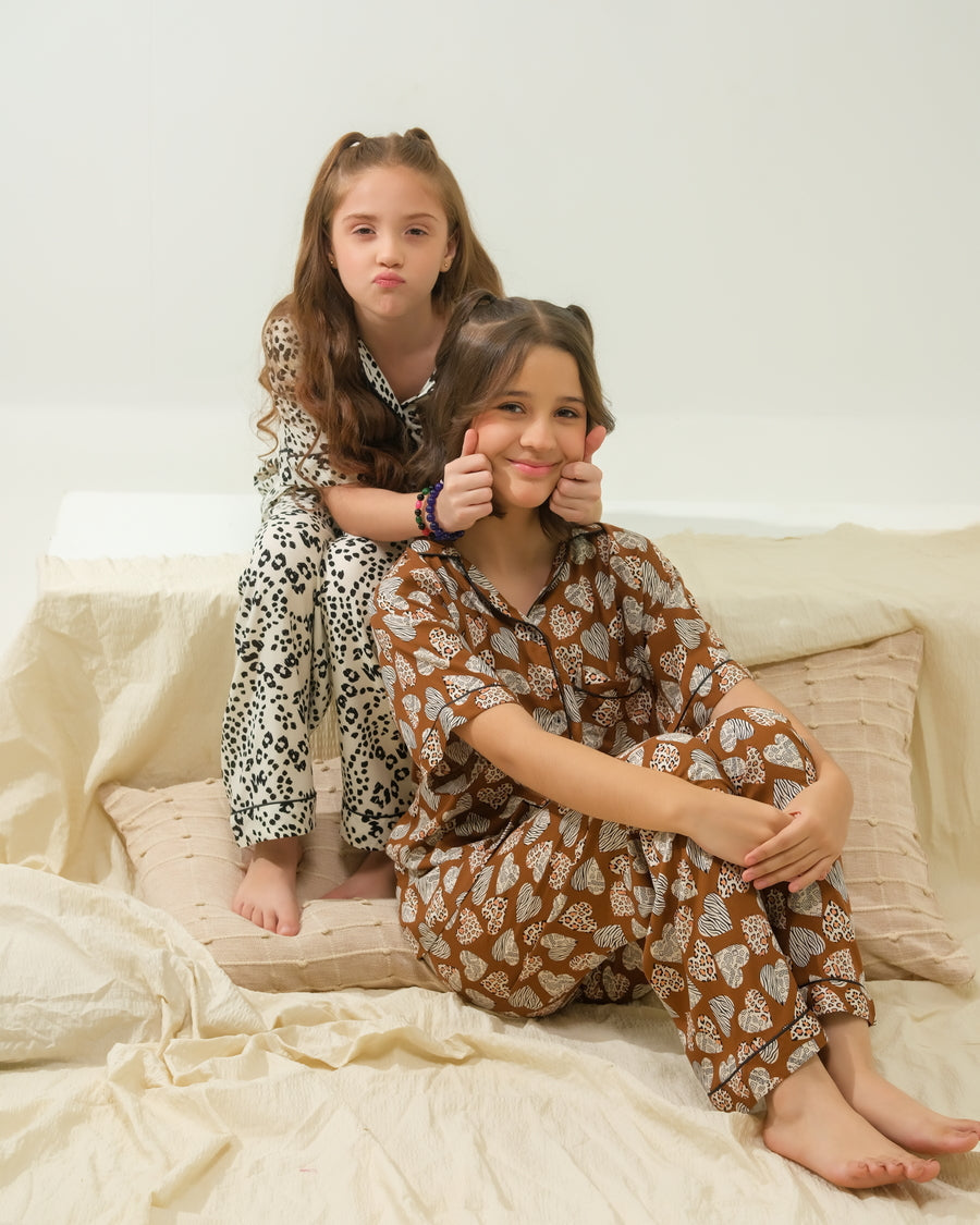 Two girls wearing printed two-piece Sprinkles night suits in a bedroom setting